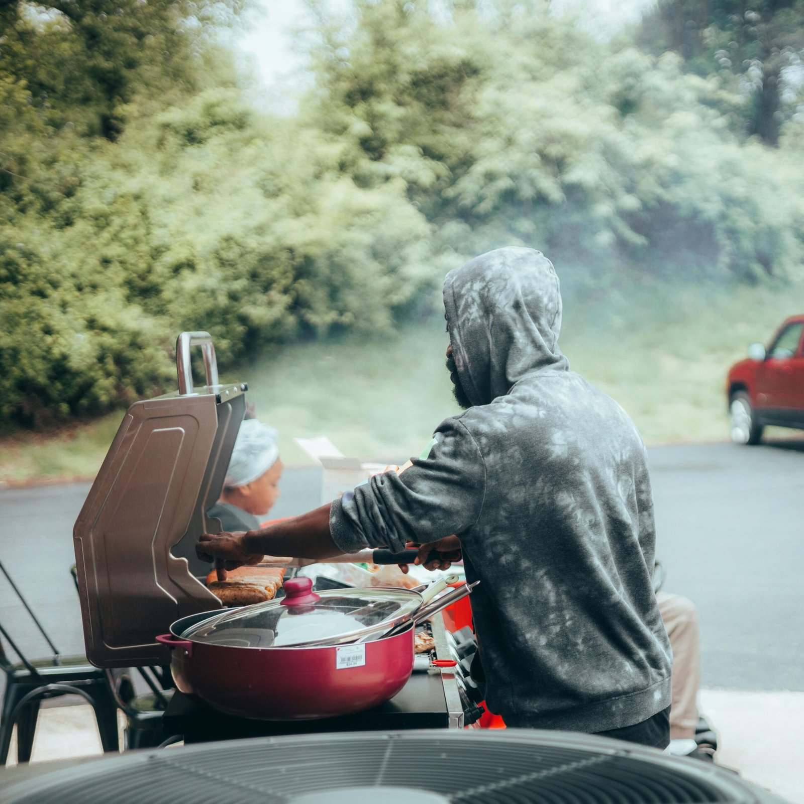 A man grilling food outdoors on a summer day, surrounded by nature and leisure vibes.