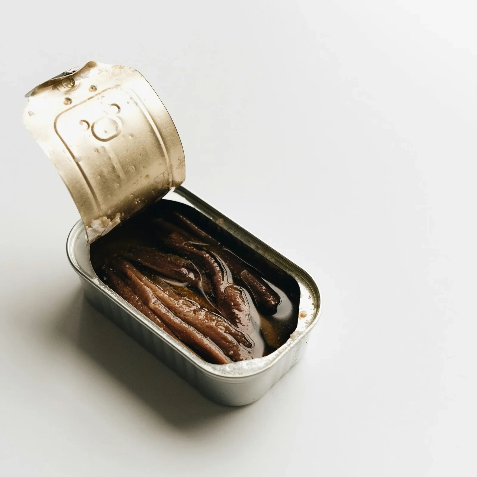A minimalist still life of an open tin containing preserved anchovies in oil.